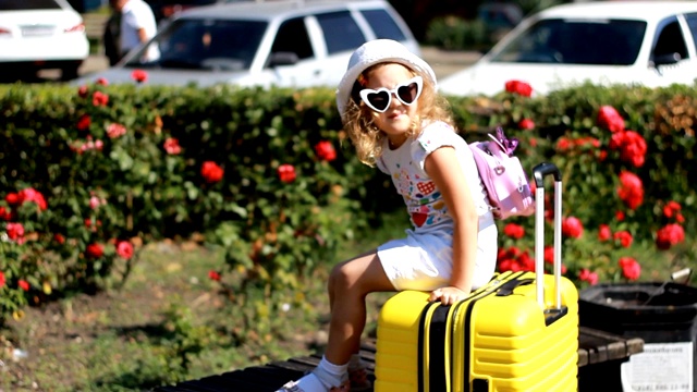 小女孩在等待旅行。快乐的儿童游客与大黄色手提箱。视频下载