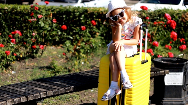 等待旅行的孩子。女游客坐在一个黄色的大行李箱上。视频下载
