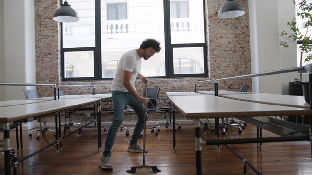 一名拉丁美洲男子戴着耳机在打扫办公室，一边听着音乐一边跳舞，一边扫地视频下载