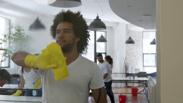 一个快乐的男人在擦窗户，一边喷肥皂一边跳舞，团队在后台打扫视频素材