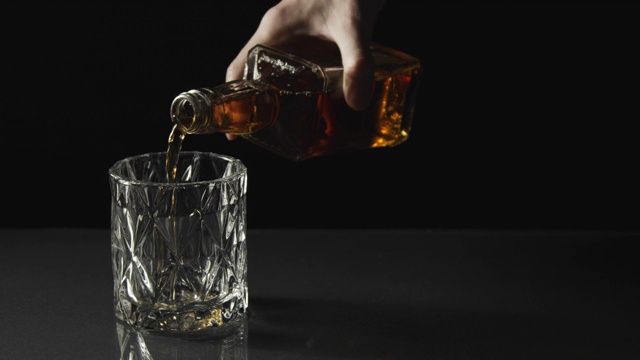 将威士忌从瓶中倒入黑色背景的玻璃中视频下载
