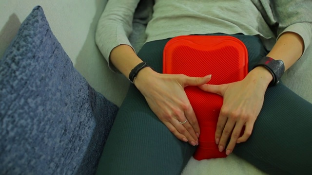 女孩把一个温暖的加热垫放在肚子上，以缓解经前症候群的症状。视频素材