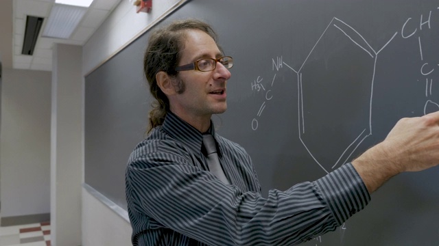 一个正在做有机化学讲座的人指着黑板上的一个公式视频下载