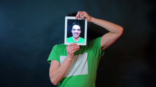 这个人拿着一个平板电脑，平板电脑的屏幕是一个人的视频肖像。视频下载