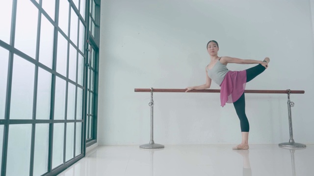泰国芭蕾舞演员在教室的栏杆前伸展。在长时间练习之后，她正在做最后的练习。视频素材
