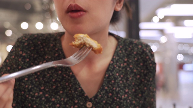 4k年轻亚洲女子用叉子吃炸鸡，自然在门里的光，坐下来吃美味的午餐，快乐，享受她的食物，约会晚餐，一人中半身拍摄，模糊的背景视频素材