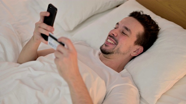 年轻人在床上用智能手机成功网购视频素材