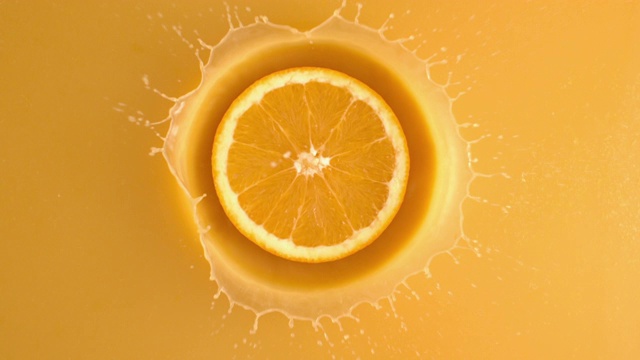 在4K慢镜头中，一片新鲜的橙子从上面扔进果汁，溅着水滴视频素材