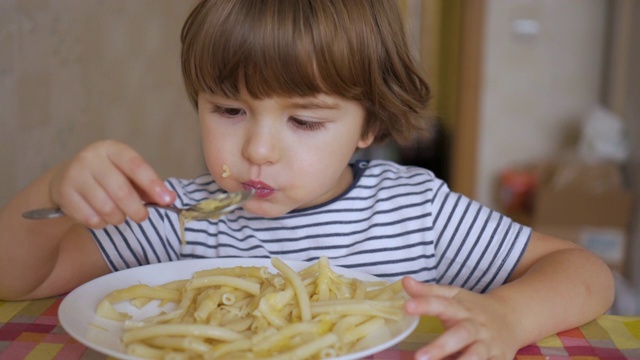可爱的小男孩在厨房吃奶酪意大利面。滑稽健康的学龄前小男孩吃面条。饥饿的孩子用手吃饭，微笑着在家吃健康食品。视频素材