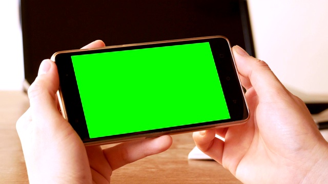 商人用绿色屏幕的手机在办公桌上进行色键拍摄视频素材