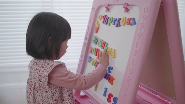 蹒跚学步的小女孩在家靠在白板上的字母视频下载