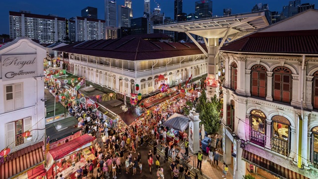 WS/TL/PD中国农历新年期间唐人街的白天到晚上的过渡/平移时间流逝，展示了一个繁忙的夜市和拥挤的街道，映衬着新加坡的天际线视频下载