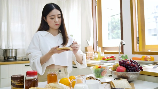 快乐的亚洲妇女在厨房的面包上涂果酱，健康的饮食和健康的概念。视频素材