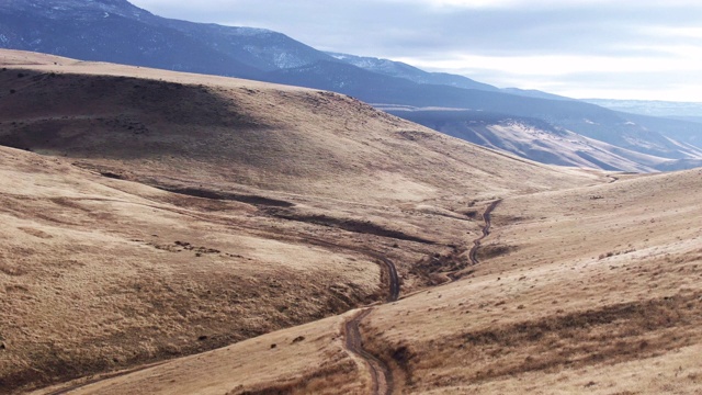 无人机拍摄的土路蜿蜒沿着一个山谷覆盖着棕色的草在科罗拉多西部户外大Mesa的基础在一个部分阴天视频下载