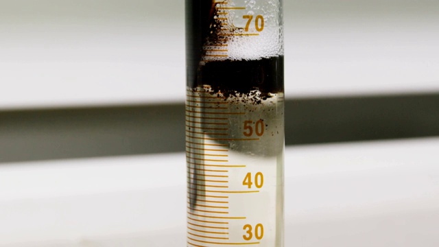 在实验室里，油倒进量杯里，浮在透明的液体上视频素材