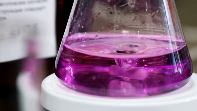 烧瓶在支架上旋转，粉红色液体变成紫色，在实验室中加入清澈的滴流视频下载