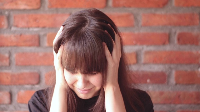 一个悲伤的黑发女人的肖像，刘海穿着黑色t恤在砖墙的背景视频素材