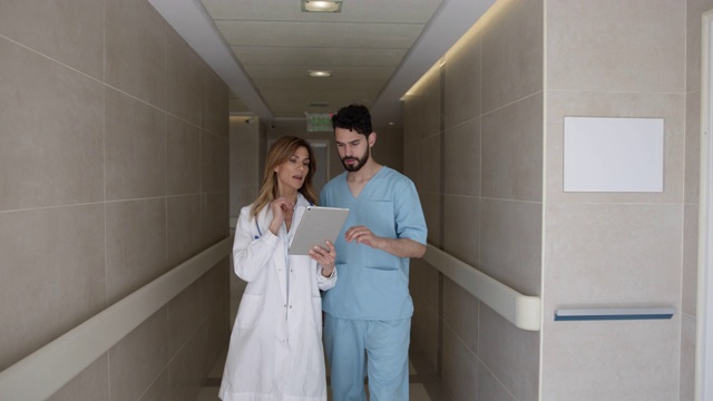 女医生和外科医生一边在医院走路一边在平板电脑上看电子病历一边讨论一个病例视频素材
