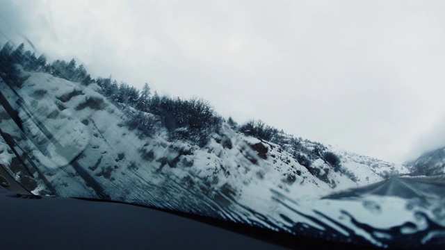 雨刷去除水和冰的特写镜头，从汽车的挡风玻璃，而驾驶在一个阴天下的冬天的雪视频素材