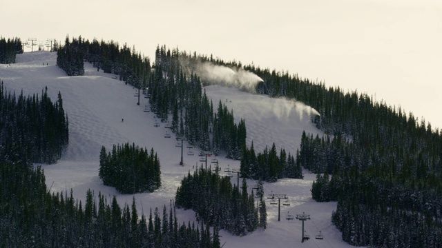 冬季日落时分，在科罗拉多山滑雪度假村，当人们滑雪和滑雪板滑下斜坡时，雪机将雪吹到空中视频下载