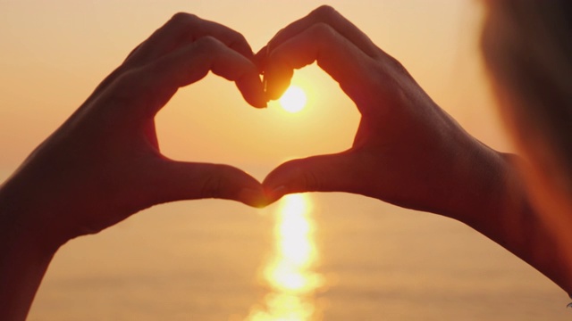 在太阳升起的海面上，女性的手呈心形。美丽浪漫的场景视频素材