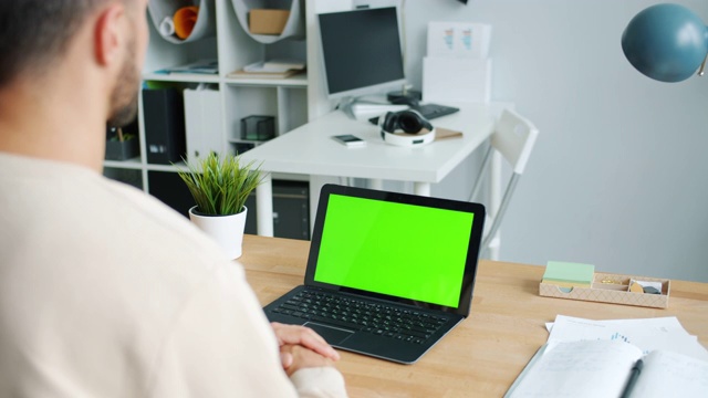 商人看着笔记本电脑与色度键绿色屏幕在办公室办公桌视频素材