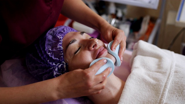 在取下抗衰老美容面膜后，美容师擦拭病人的面部。视频下载