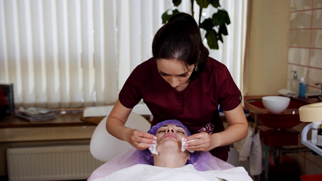 美容师在手术前用棉签擦拭女性患者的面部，消毒。视频下载