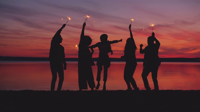 朋友们拿着燃烧的火花在海滩上跳舞，享受户外派对视频素材