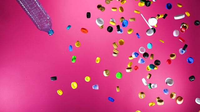 多色塑料瓶盖和塑料瓶落在粉红色的背景视频素材