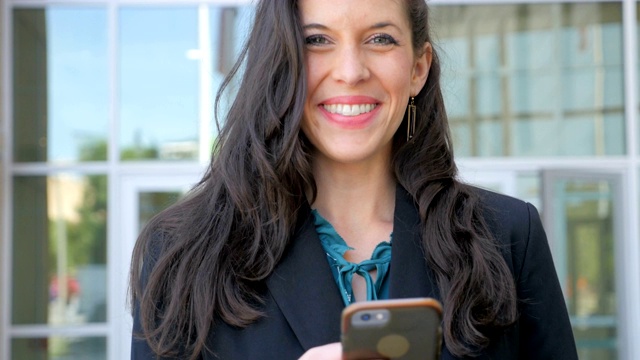一位穿着考究的女士在她的智能手机上抬头对着镜头微笑视频素材