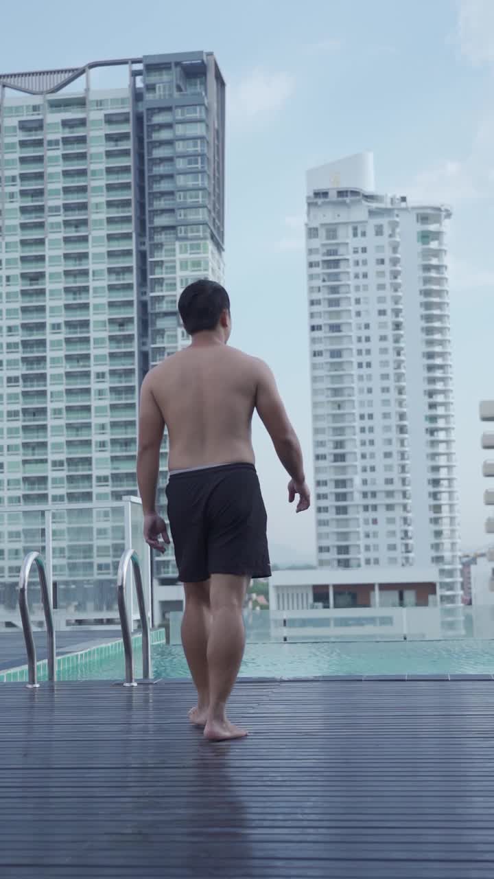 SLO MO -以建筑物为背景的一个年轻人跳进游泳池的垂直镜头视频素材