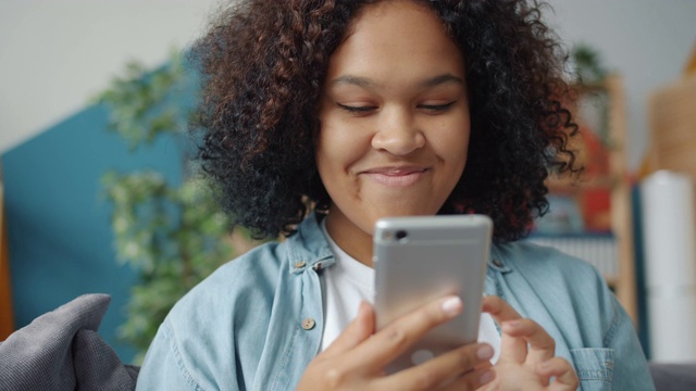 漂亮的美国黑人女士在家里用智能手机发短信微笑视频素材
