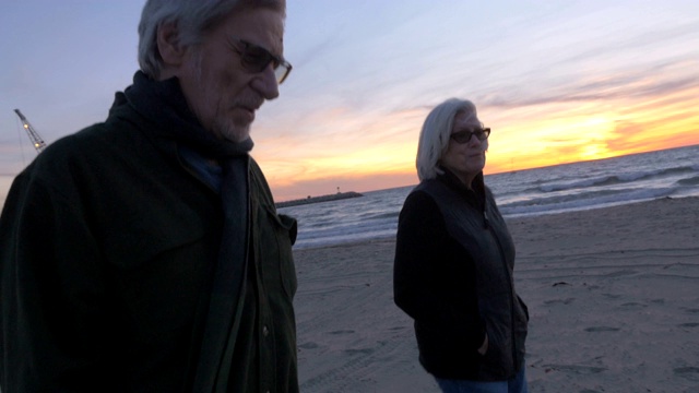 健康快乐微笑的60岁老人夫妇在海滩上散步日落视频下载