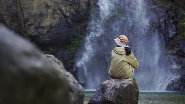 女人坐在岩石上看瀑布落下视频素材