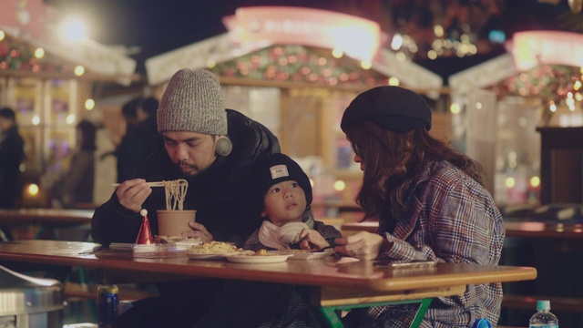 年轻的家庭享受街头食品在圣诞市场的夜晚在冬天视频下载