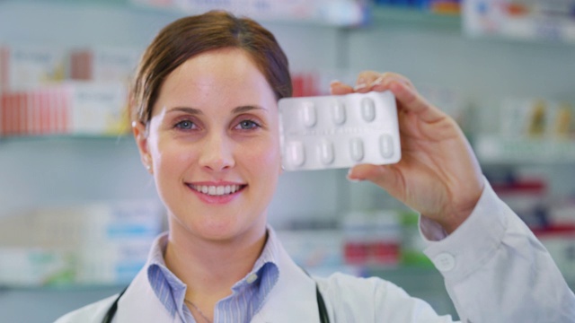 一名年轻女性药剂师顾问在镜头前微笑着展示一包药丸的慢镜头视频素材