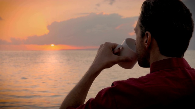 一个男人一边喝着咖啡，一边欣赏着大海上美丽的日出视频素材
