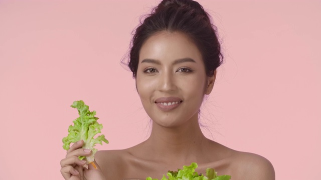 特写美丽的年轻亚洲女人与完美光滑健康的皮肤吃沙拉对粉红色的背景。护肤商业概念。视频素材