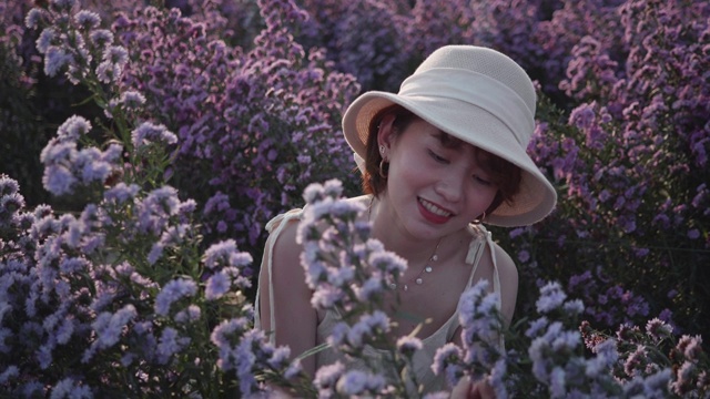 在一个阳光明媚的日子里，一位年轻女子轻轻地把花捧在手里，闻着紫色的花。慢动作视频素材