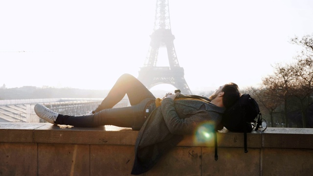 快乐的男游客躺在史诗般的日落埃菲尔铁塔在巴黎在秋季假期慢动作。视频素材