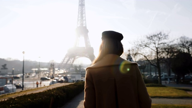 镜头跟随快乐放松的美丽女子走在背光阳光下的秋天巴黎埃菲尔铁塔慢镜头。视频素材