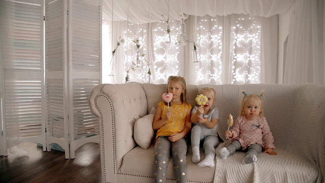 三姐妹的女孩坐在舒适的沙发上吃糖果视频下载