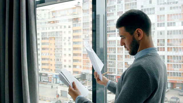 年轻的商人在现代办公室的窗户旁阅读金融研究的肖像视频素材