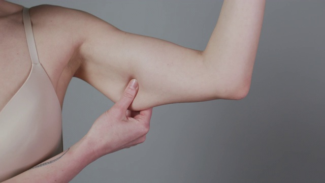 减肥的概念。胖女人捏上臂脂肪孤立在灰色背景。特写白种人女性的手检查松弛的皮肤。控制身体，是时候节食了视频下载
