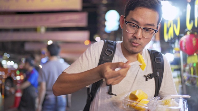 旅游男子吃芒果糯米是一种传统的泰国甜点，由糯米、新鲜芒果和椰奶制成，用勺子或有时用手吃。视频素材