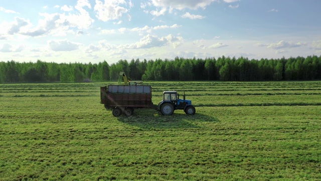 收割机收集割下的草，并把它倒进拖拉机拖车空中侧面视图视频素材