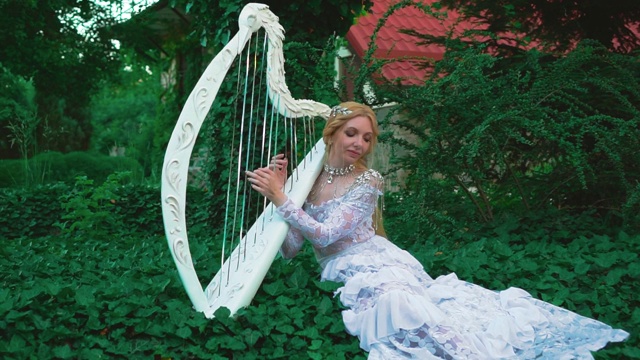 迷人的金发女子在一个白色，创意，蕾丝复古连衣裙演奏竖琴视频素材