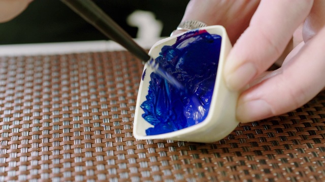 一个女人用画笔混合蓝色颜料的特写。4 k视频下载