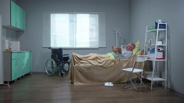 一个男人躺在医院的床上，在平板电脑上看一些东西视频素材
